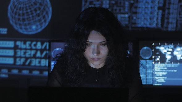 Portrait of Young Woman Programmer Working at a Computer in the Data Center Filled with Display