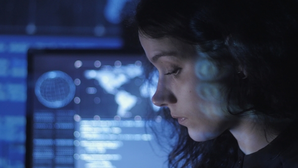 Portrait of Young Woman Programmer Working at a Computer in the Data Center Filled with Display