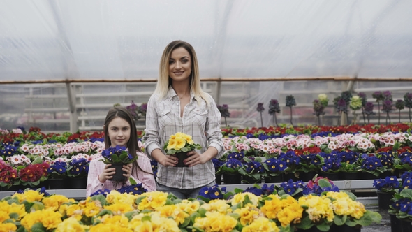 Smiling Adult and Young Girls Stretching Flower Pots to Camera