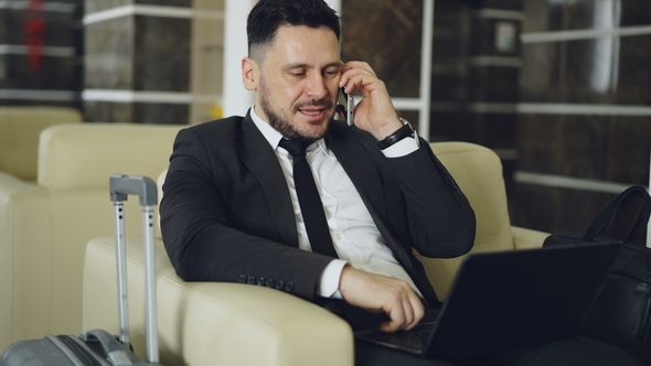 Tilt Up of Confident Businessman Talking Mobile Phone and Using Laptop Computer While Sits on