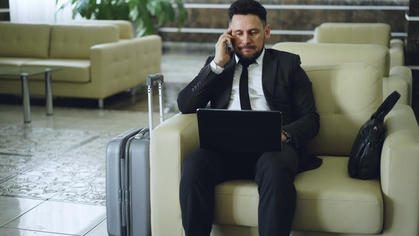 Tilt Up of Confident Attractive Businessman Talking Mobile Phone and Using Laptop Computer While