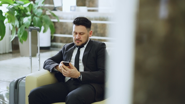 Bearded Concentrated Businessman Using Smartphone Sit on Armchair Inside Luxury Hotel After Arrivel