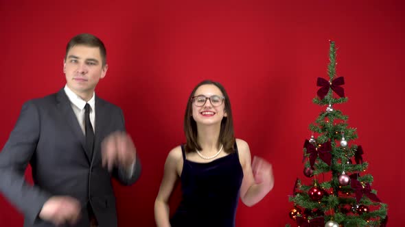 Young Man and Woman Dancing Near the Christmas Tree. A Man in a Suit and a Woman in a Dress on a Red