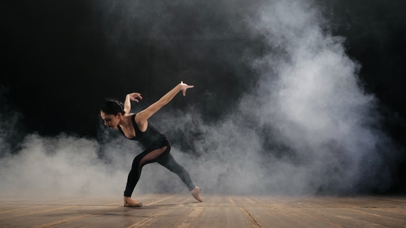 Young Beautiful Ballerina on Smoke Stage Dancing Modern Ballet in the Dark. Woman in Black Costume