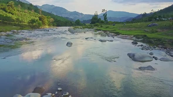 Flycam Moves Above River Against Natural Landscape on Sunny Day