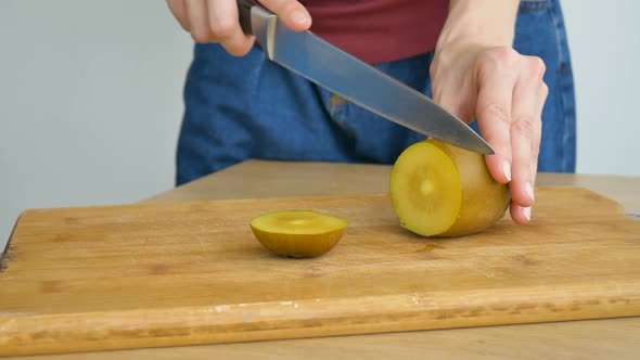 Female Hands is Cutting a Fresh Ripe Golden Kiwi Fruit on a Cut Wooden Board