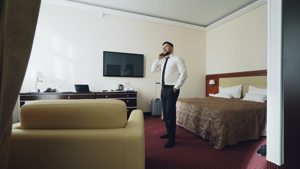 Confident Businessman Talking on Mobile Phone While Walking Around Hotel Room. Travel, Business and