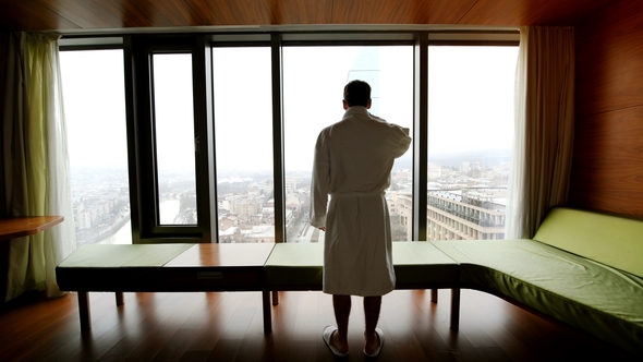 Man in Bathrobe Drinking Coffee in the Morning, Stretching and Looking at Cityscape