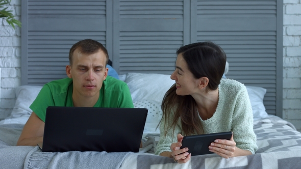 Happy Couple Networking with Digital Devices on Bed