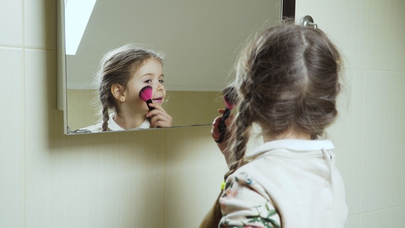 Cute Little Girl Applies Powder on Her Face with Brush in Front of Mirror