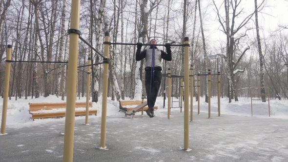 Fitness Man Training Pull Up Exercise on Sport Ground. Outdoor Winter Training