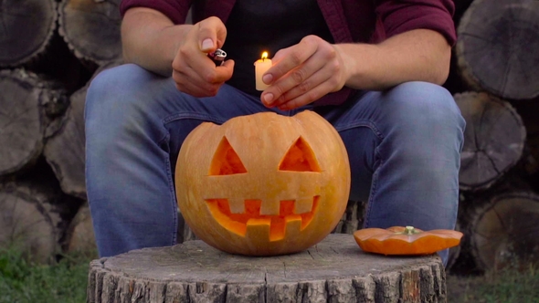 A Man Puts a Burning Candle in Jack's Lantern. In the Backyard on the Stump
