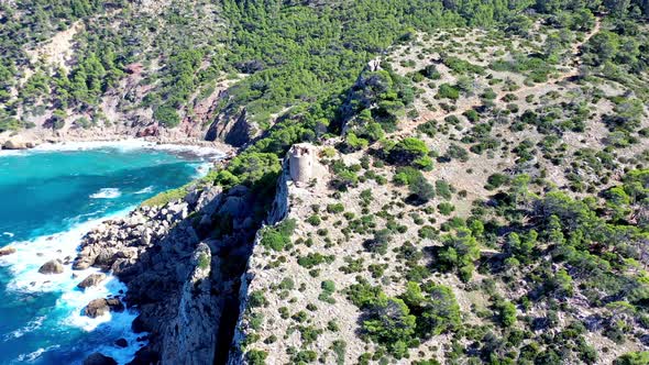 Basset Cove in Mallorca Spain with tower overlooking the blue cove below, Aerial dolly out reveal sh