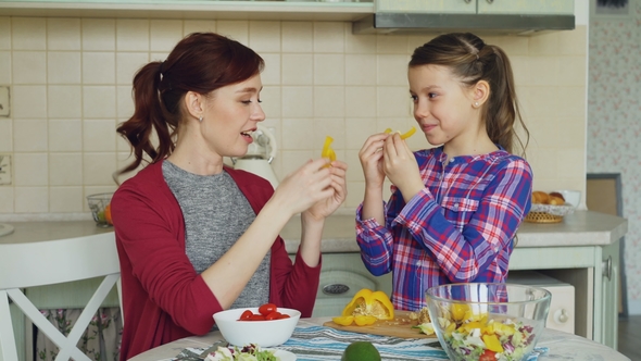 Joyful Mother and Cute Cheerful Daughter Have Fun Grimacing Silly with Vegetables While Cooking in
