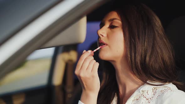 View of Pretty Longhaired Girl Applying Lipstick at Car Front Mirror