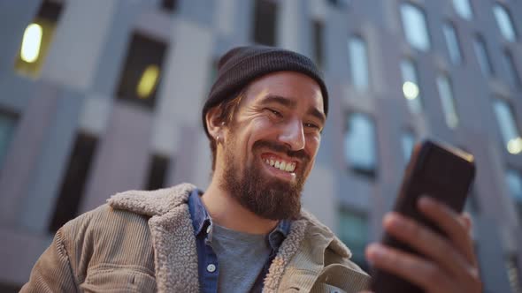 Laughing man wearing hat showing building to phones camera