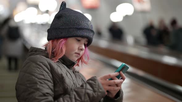 A Young Beautiful Teenage Girl is Climbing Into the Subway Using a Smartphone with the Internet to