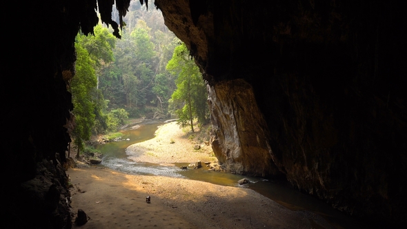 Older Woman Is Collecting Bat Guano on the Bottom of Big Cave with River Flowing From the Bowels