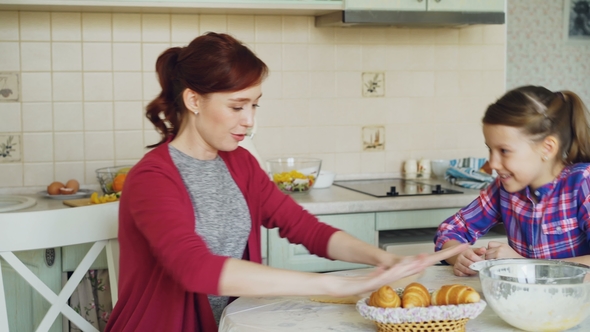 Young Mother Rolling Dough and Talking To Little Cute Daughter While Cooking in the Kitchen on