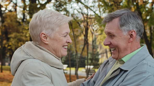 Side View Loving Old Married Couple Hugging in Autumn Park Smiling Looking at Each Other Happy