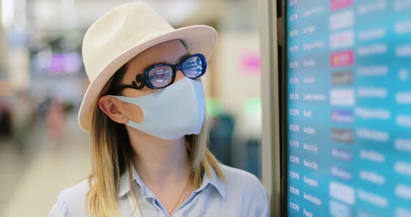 Caucasian Woman Wears Protective Face Mask Looking at Flight Schedule in Airport