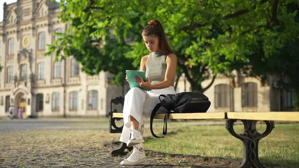 Wide Shot Portrait of Concentrated Beautiful Young Caucasian Woman Sitting with Tablet on University