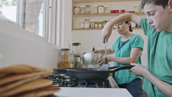 Boy preparing pancakes with his mother for breakfast in the kitchen