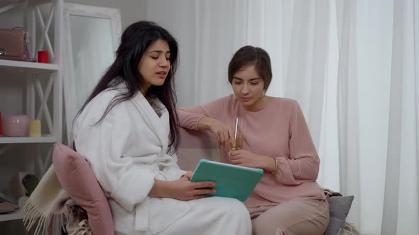 Zoom in Two Positive Young Middle Eastern Women Talking Surfing Internet on Tablet
