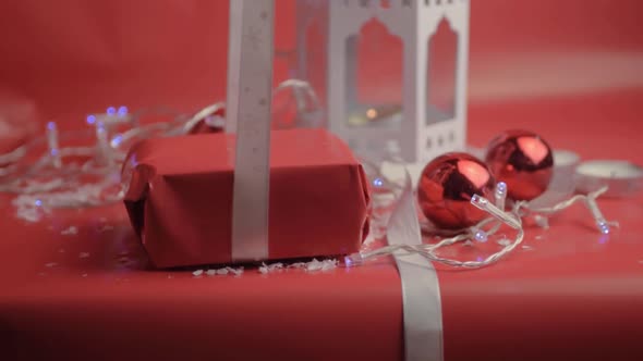 Wrapping Christmas gift with ribbon and red paper with red background and baubles