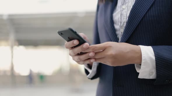 Close up Asian businesswoman in a black suit is using a smartphone.