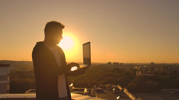 Hacker Using Laptop on Rooftop with City View and Forex Chart. Hacking and Stats Concept