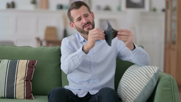 Broke Young Man Checking Empty Wallet on Sofa 