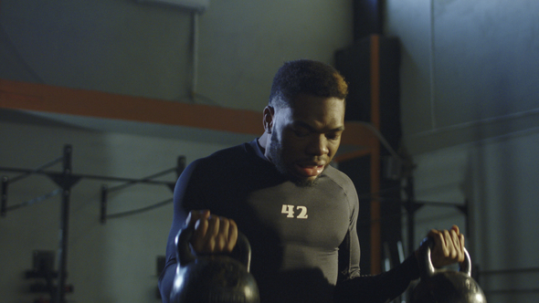 Strong Black Man Lifting Kettlebells in Gym
