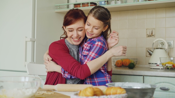 Cheerful Mother Cooking in the Kitchen While Cute Daughter Coming and Embracing Mom in the Morning