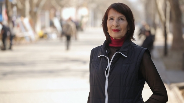 A Stylish Woman in a Sportive Jacket Stands in an Alley on a Sunny Day