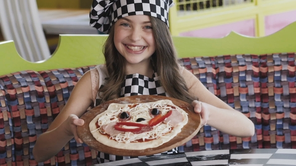 The Young Girl Shows a Pizza with Smiles at Camera