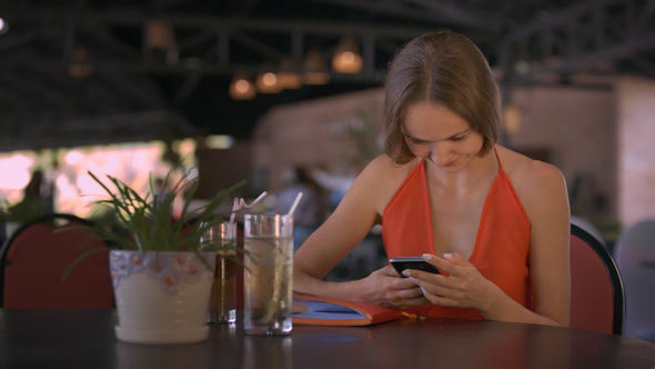 Girl Surfs Internet Using Smartphone Sits at Table