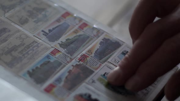 Extreme Closeup of Unrecognizable Senior Man Adjusting Postage Stamps at Collection Book in Dark