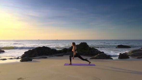 Blond Girl Practices Yoga on Beach by Sea and Rock