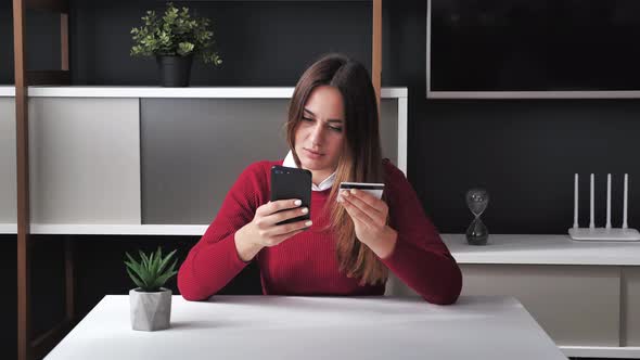 Smiling Young Woman Customer Holding Credit Card and Smartphone Sitting at Office