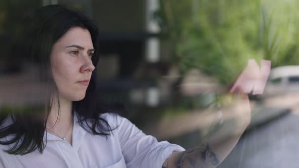 Concentrated Smart Woman Sticking Adhesive Notes on Window Glass Planning Business Indoors