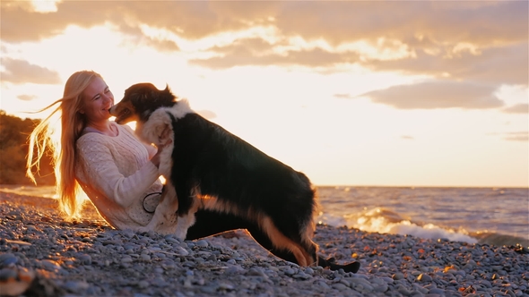 Young Woman Playing with Australian Shepherd on the Shores of a Lake or the Sea.