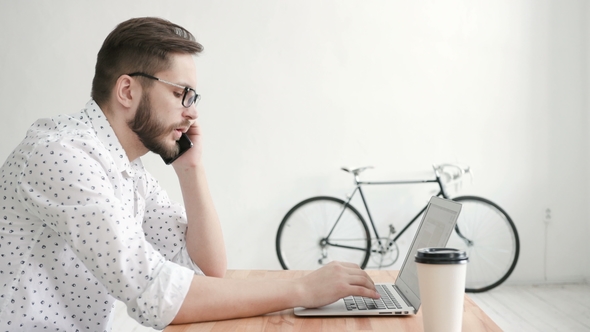 Man in Office Talking at Phone and Type at Laptop