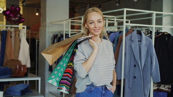 Attractive Young Woman Standing with Many Paper Bags in Clothing Store, Smiling Happily