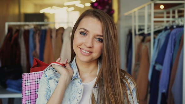 Attractive Young Girl Standing with Paper Bags in Clothing Shop and Looking at Camera