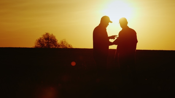 A Firm Handshake of Two Farmers on the Field. They Communicate, Use a Tablet. At Sunset
