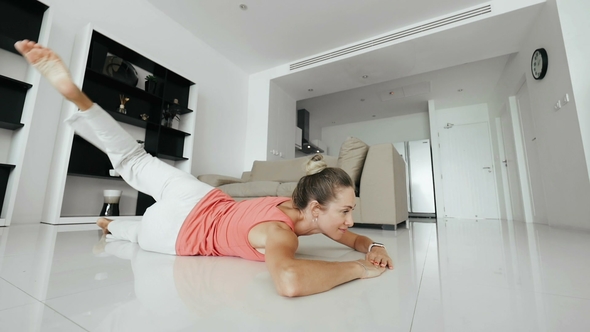 Beautiful Woman Doing Fitness Exercise Lying on Floor and Raising Leg Up in Home