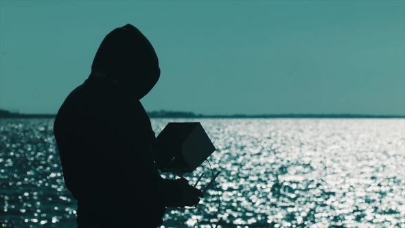 Silhouette of Man in Hood Using Radio Controller on Lake Shore