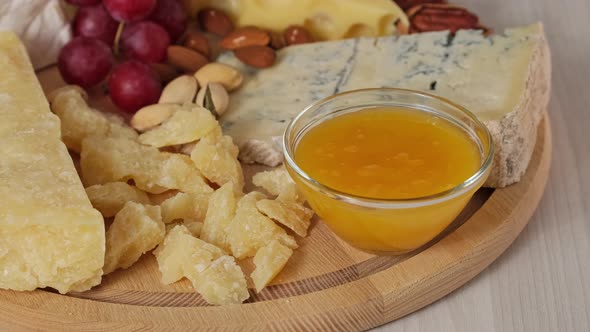 Preparation of cheese plate with hard cheeses camembert, brie, parmesan, dutch cheese, grapes, honey