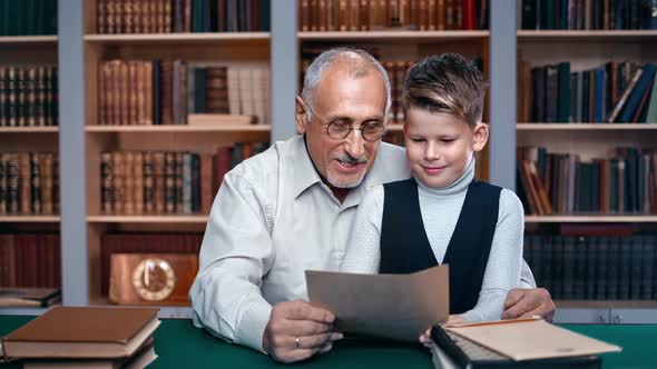 Cheerful 70s Elderly Man Male Kid Reading Vintage Letter Paper Sheet Sitting at Table Desk Library